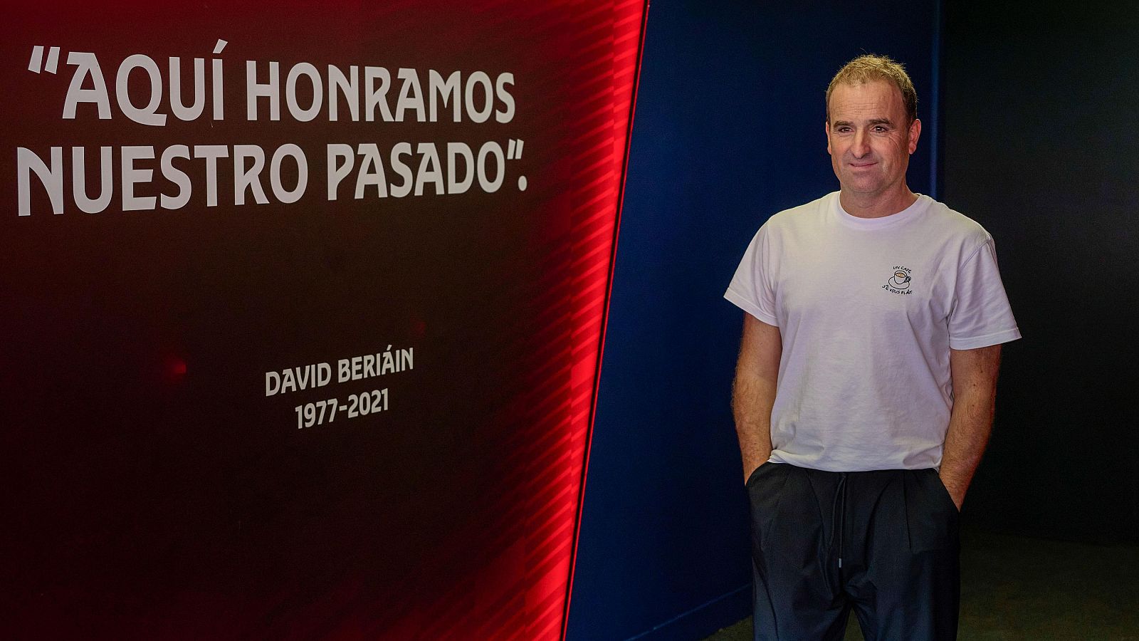 El entrenador Jagoba Arrasate posa en un pasillo junto a un panel conmemorativo dedicado a David Beriáin en un entorno con los colores de Osasuna.
