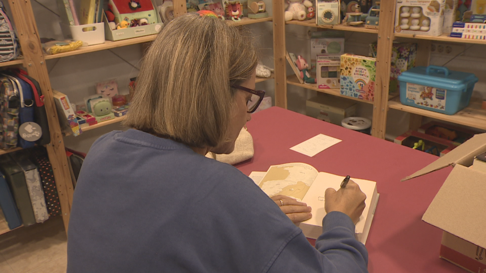 Una mujer escribe una dedicatoria en un libro que llegará a una mujer que está en prisión
