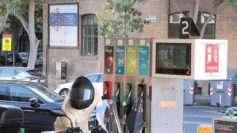 Motorista repostando en un surtidor de gasolina de una estación de servicio urbana en Zaragoza junto a un edificio de ladrillo.