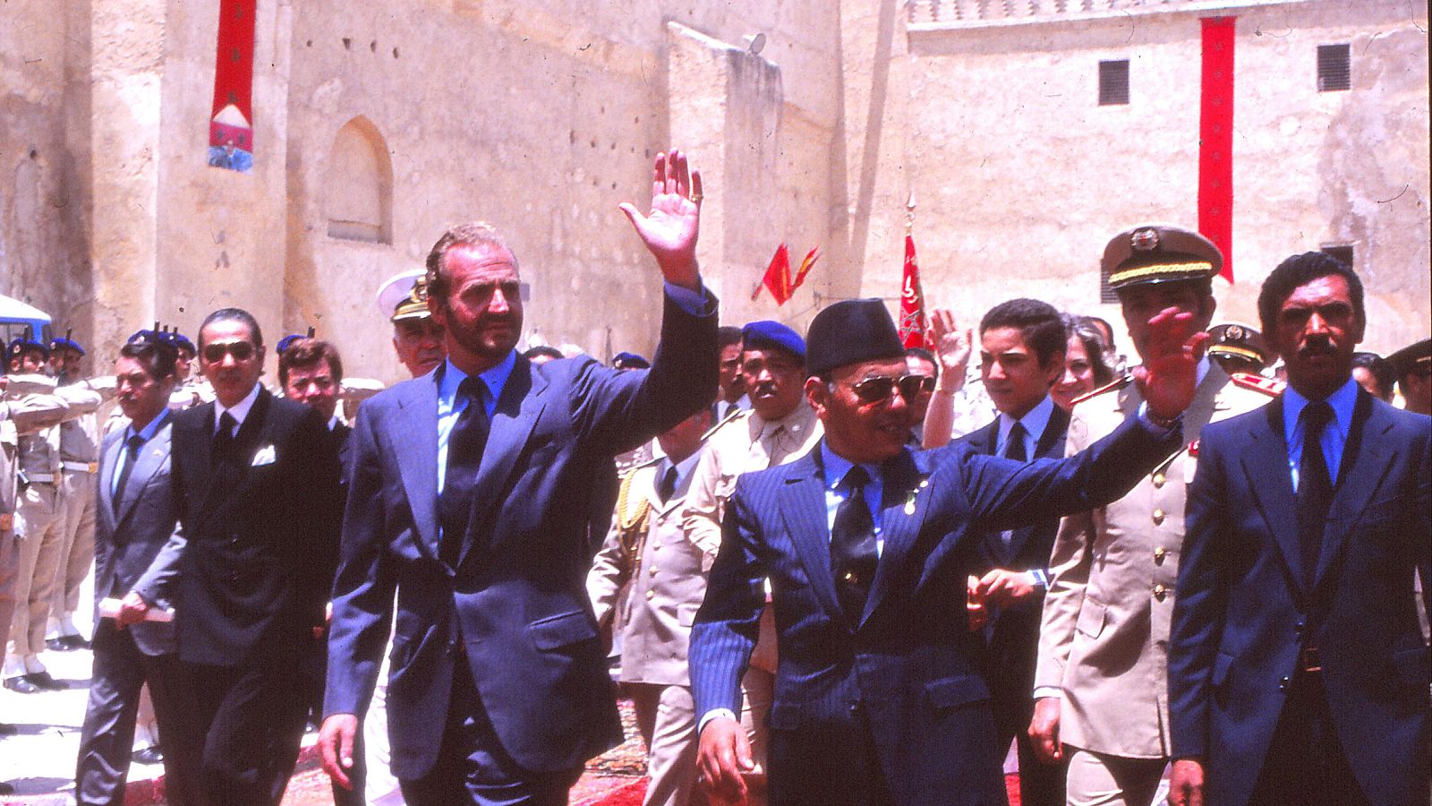 Fotografía histórica de los reyes Juan Carlos I y Hasán II caminando juntos en un patio palaciego durante una visita oficial en 1979, rodeados por su comitiva.