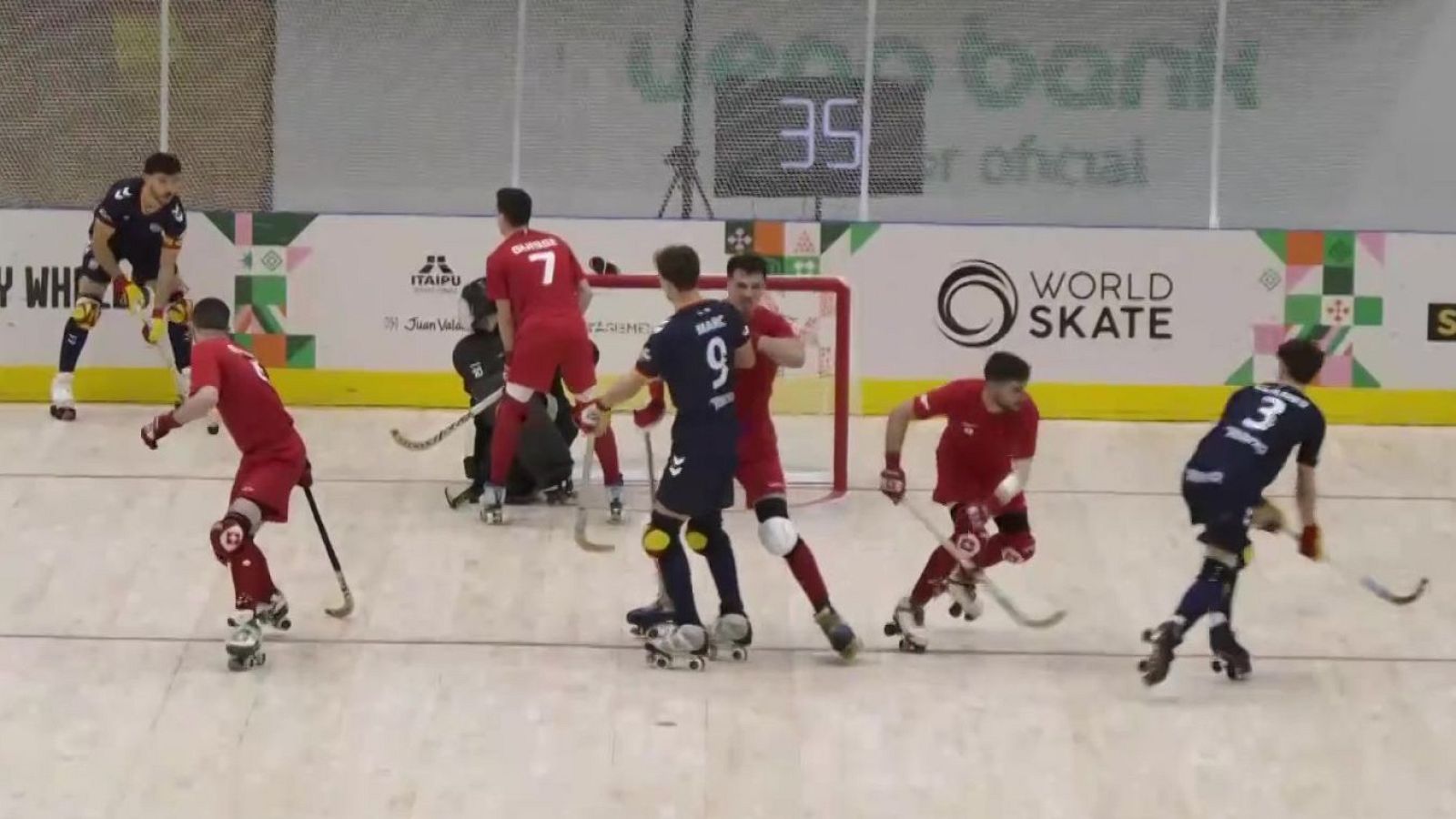 Intensa jugada de hockey sobre patines con jugadores de España y Suiza forcejeando frente a la portería en una pista cubierta.