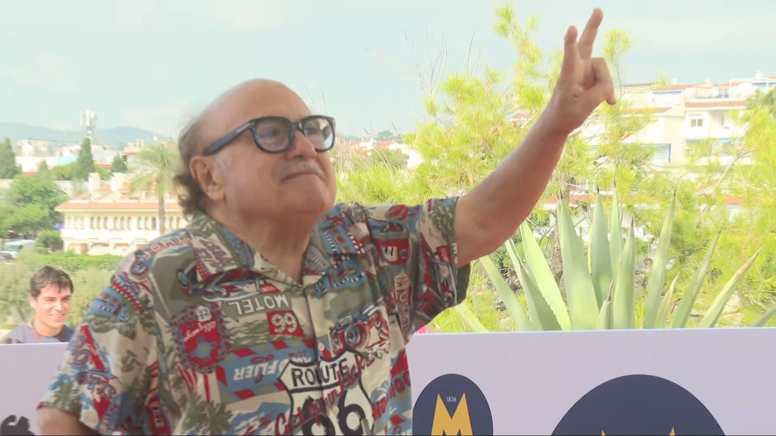 Danny DeVito somriu i fa el senyal de la victòria amb la mà en un photocall a l'aire lliure.