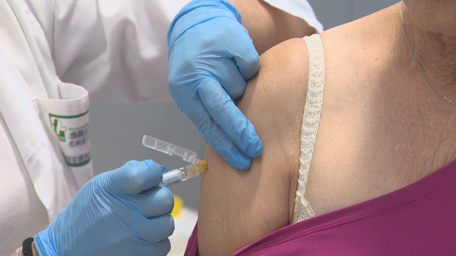 Primer plano de un profesional sanitario administrando una vacuna en el brazo de una paciente en una consulta médica.
