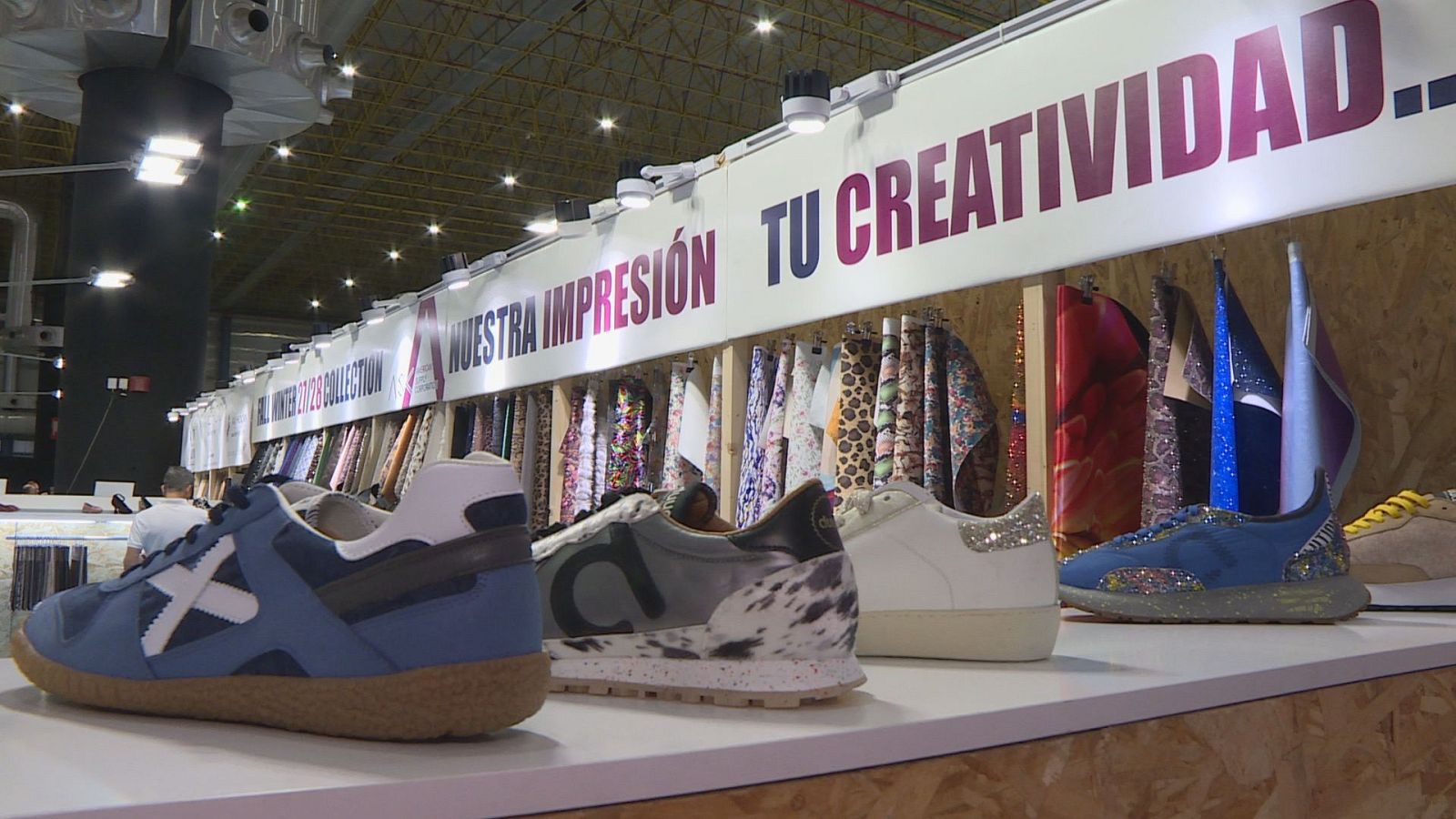 Mostrador expositor con zapatillas deportivas de diseño y muestrario de materiales y pieles en una feria de calzado.