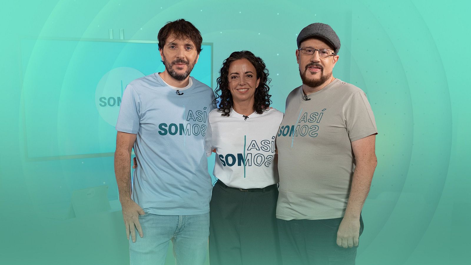 Tres personas posan sonrientes en el plató con fondo verde azulado y círculos concéntricos, vistiendo camisetas con el logotipo del programa y micrófonos de solapa.