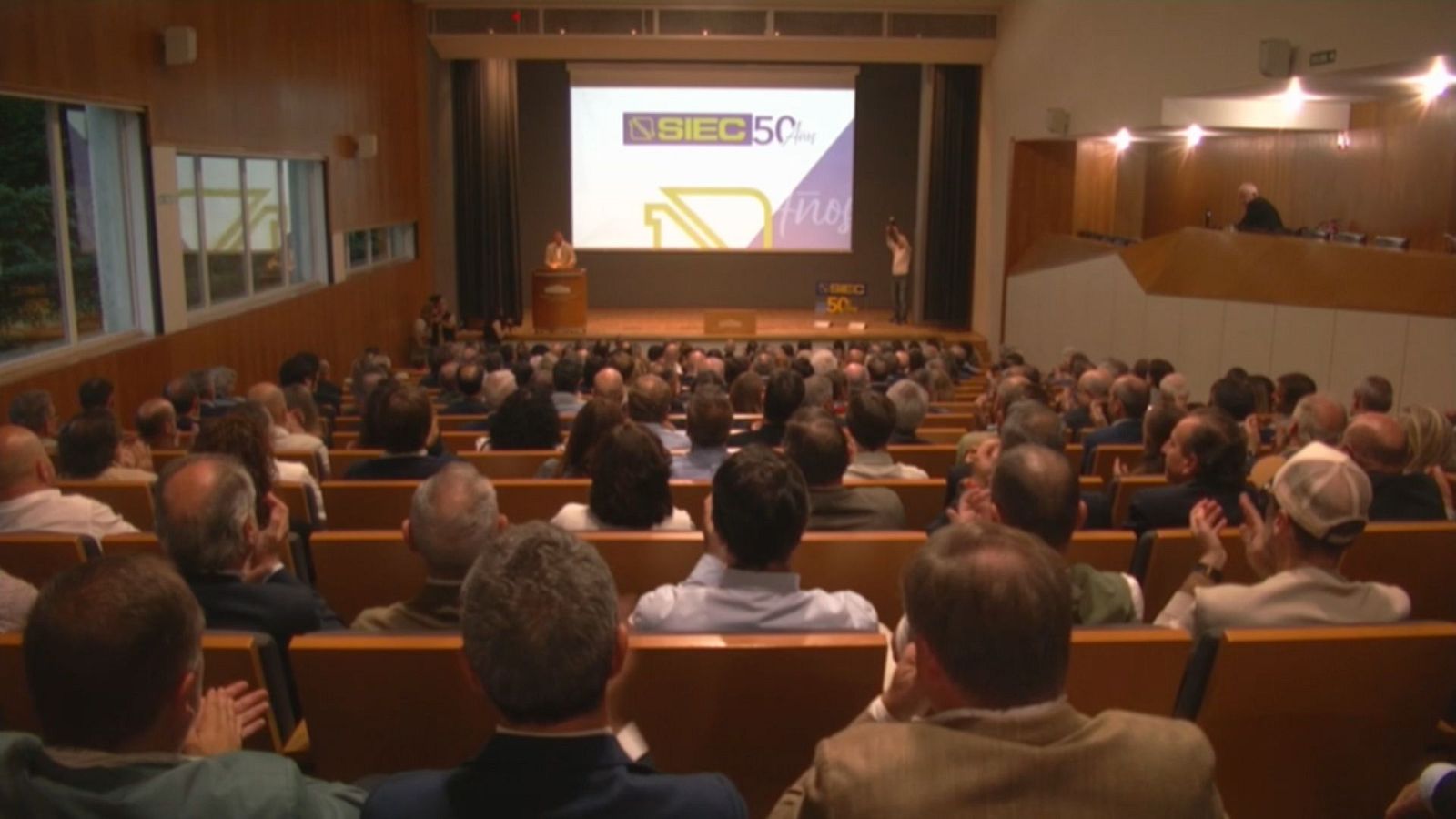 Auditorio lleno durante un evento corporativo con una pantalla en el escenario que muestra el logotipo de un 50 aniversario.