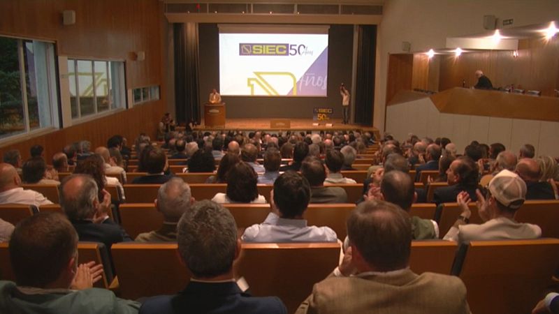 Auditorio lleno durante un evento corporativo con una pantalla en el escenario que muestra el logotipo de un 50 aniversario.