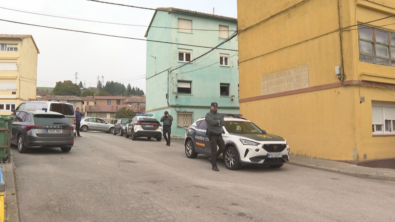 Calle residencial con un vehículo patrulla SUV de la Guardia Civil y un agente uniformado vigilando en primer plano.