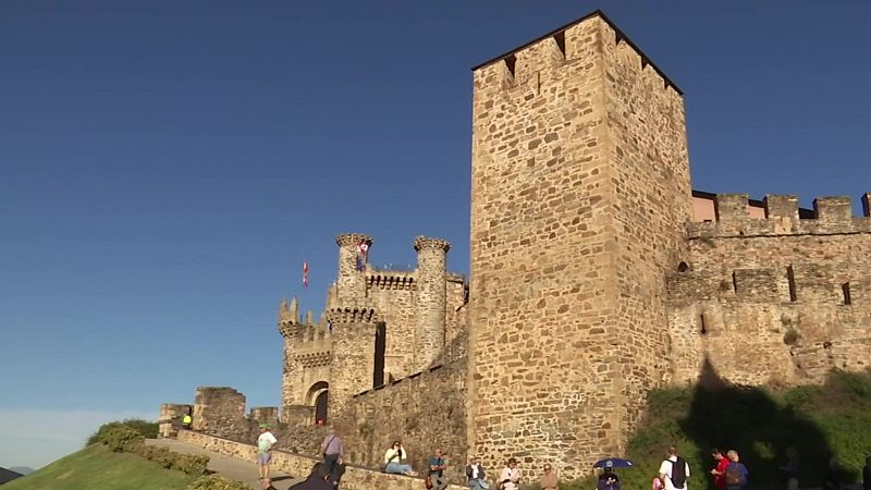 Vista exterior del Castillo de los Templarios en Ponferrada con su imponente torre, murallas almenadas y visitantes en el camino de acceso bajo un cielo azul.