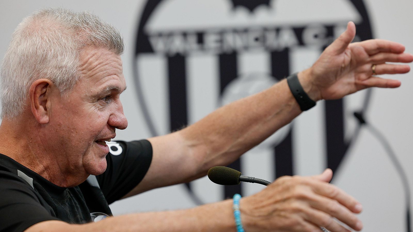 El entrenador Javier Aguirre gesticula durante una rueda de prensa frente a un micrófono, con el panel del Valencia C.F. al fondo.