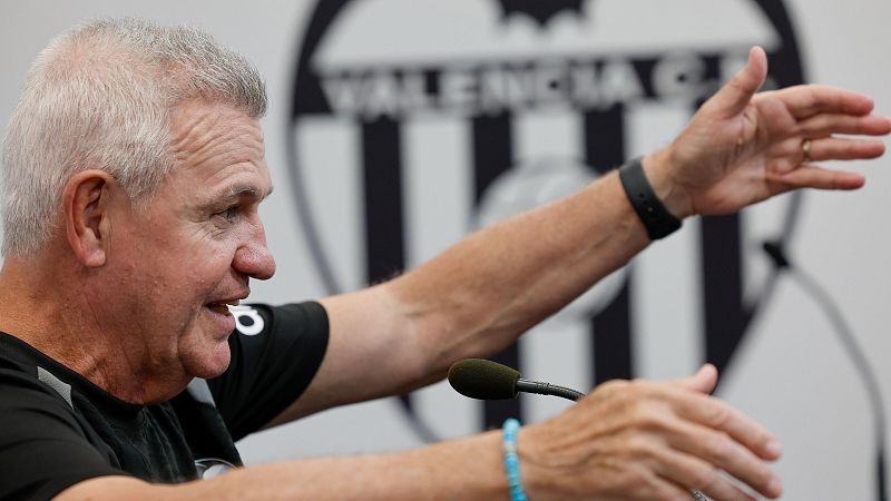 El entrenador Javier Aguirre gesticula durante una rueda de prensa frente a un micrófono, con el panel del Valencia C.F. al fondo.