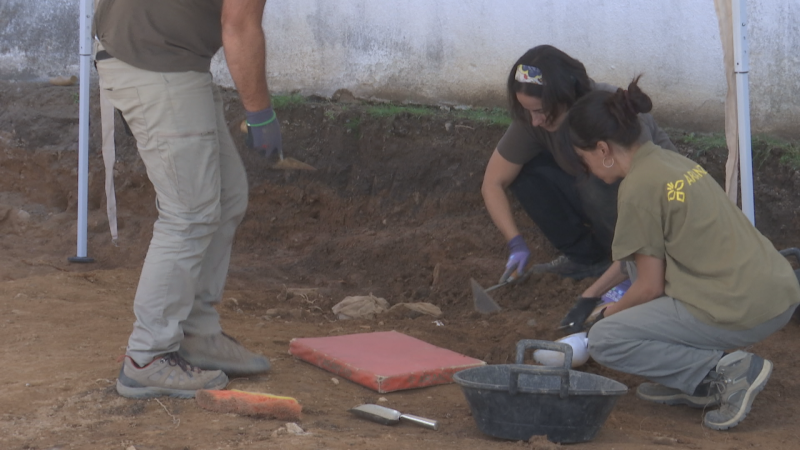 Tres especialistas en arqueología realizan labores de exhumación en una fosa común al aire libre, utilizando herramientas de excavación sobre un terreno de tierra.