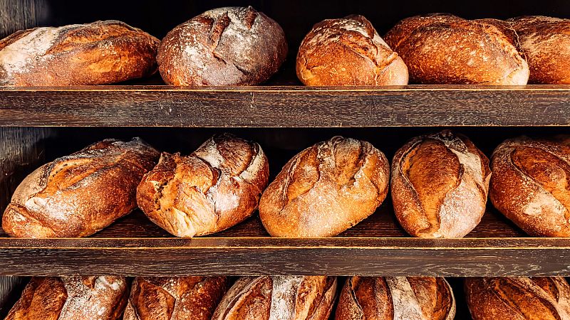 Expositor de panadería con tres estantes de madera oscura repletos de hogazas de pan rústico con cortezas tostadas.