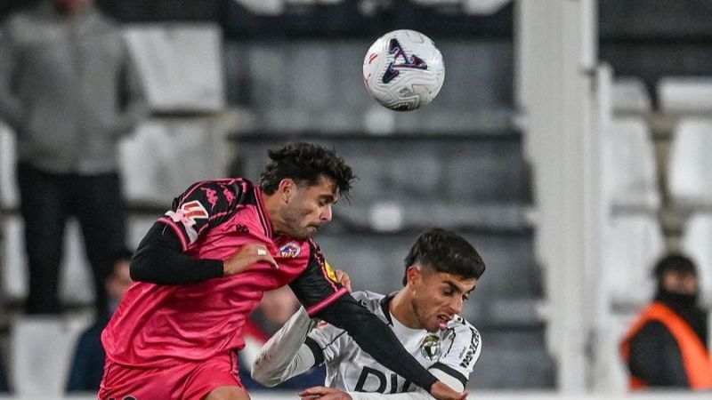 Dos futbolistas disputan intensamente un bal�n a�reo de cabeza en un partido, mostrando gran esfuerzo f�sico y concentraci�n.