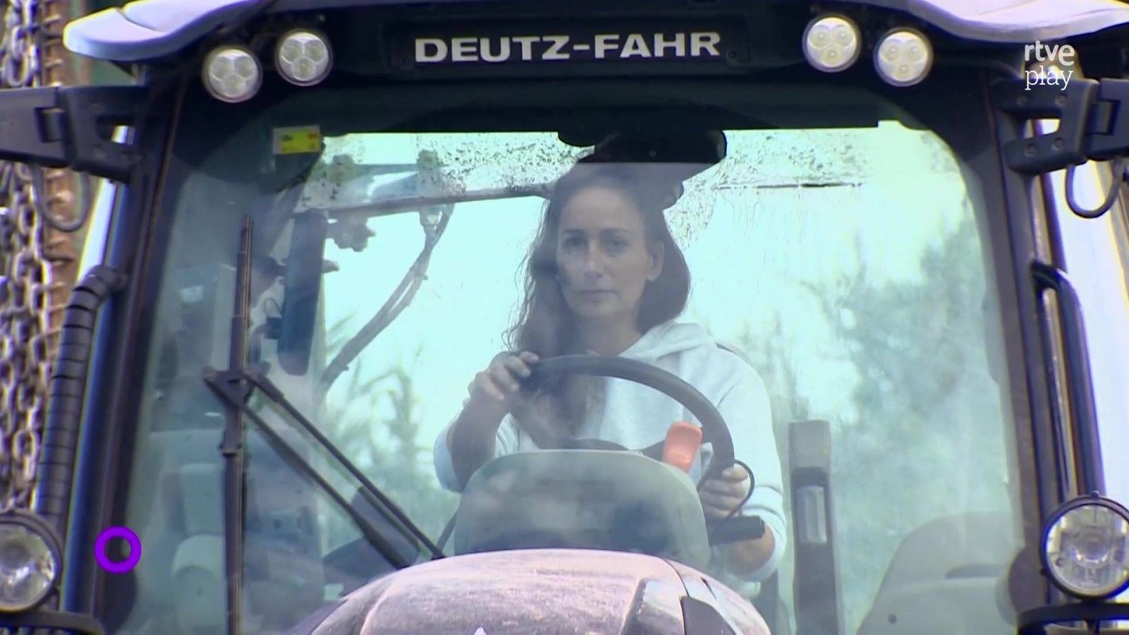Mujer al volante de un tractor DEUTZ-FAHR, mirando al frente con sudadera blanca.