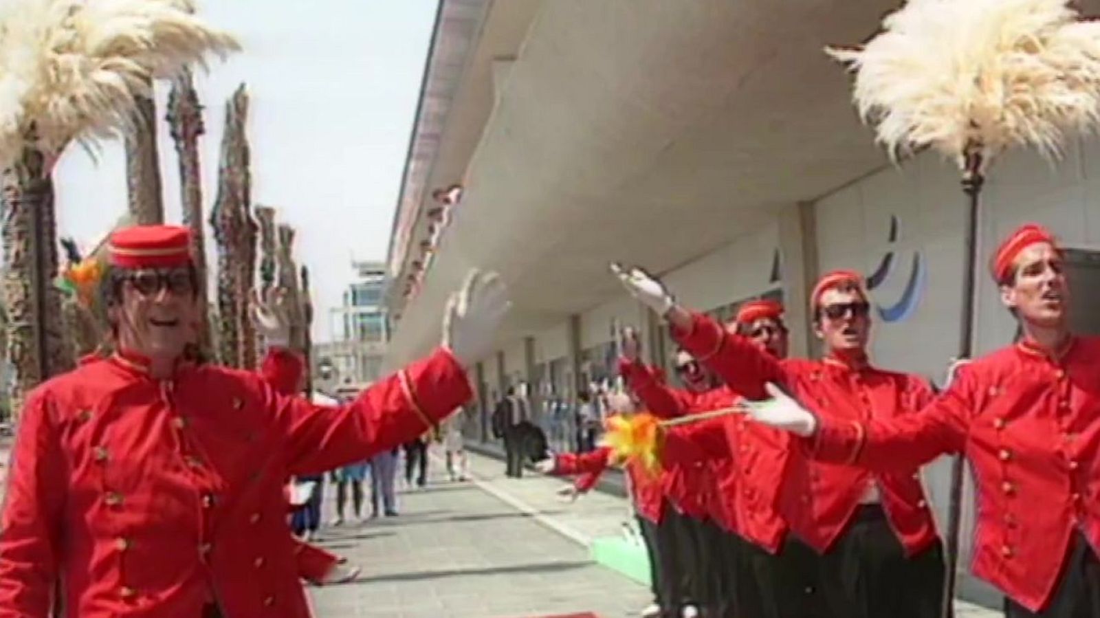 Actores disfrazados de botones clásicos con uniformes rojos y plumeros blancos realizan una animada actuación exterior.