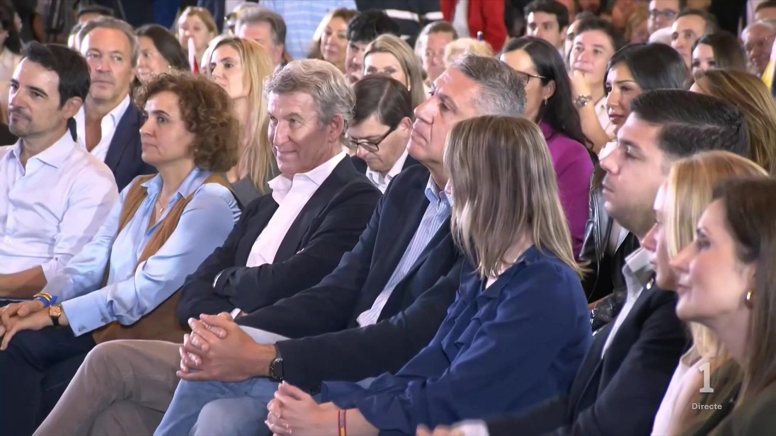 Alberto Núñez Feijóo sentado en primera fila junto a Xavier García Albiol y Dolors Montserrat en un mitin político con público al fondo.