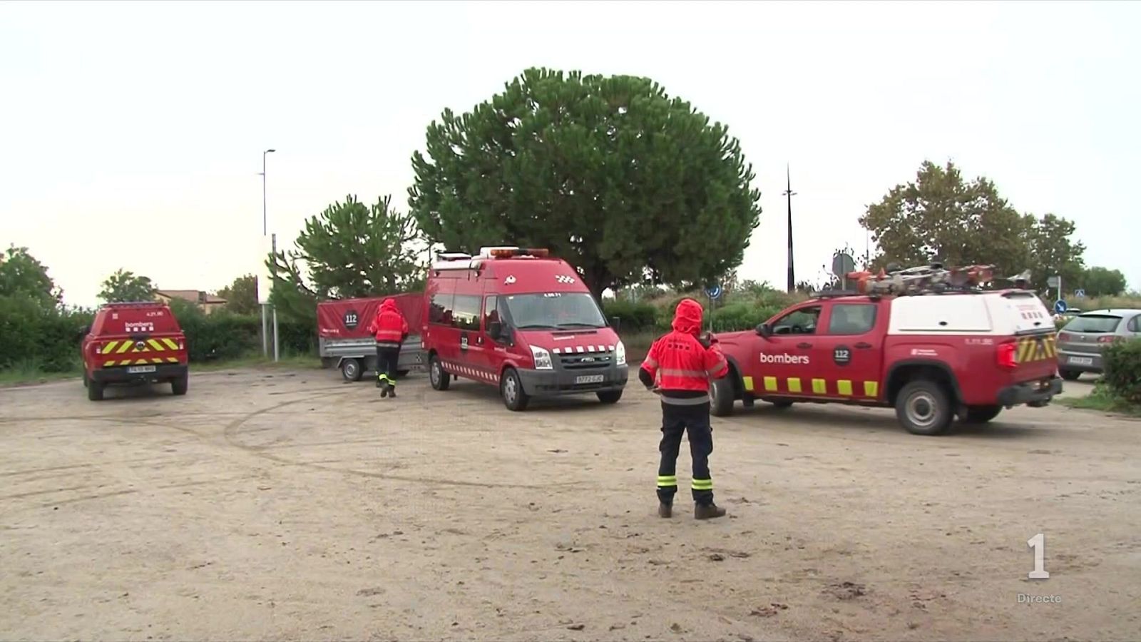 Despliegue de los Bomberos de la Generalitat con vehículos de emergencia rojos y remolque en un terreno despejado bajo un cielo cubierto.