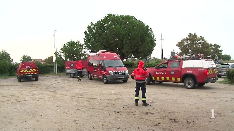 Despliegue de los Bomberos de la Generalitat con vehículos de emergencia rojos y remolque en un terreno despejado bajo un cielo cubierto.