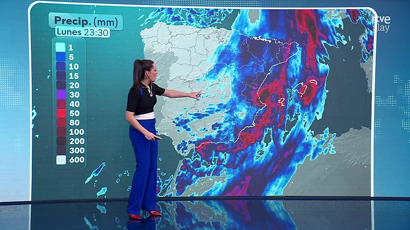 Presentadora del tiempo en un plató frente a una pantalla curva que muestra un mapa de precipitaciones con lluvias en el Mediterráneo.