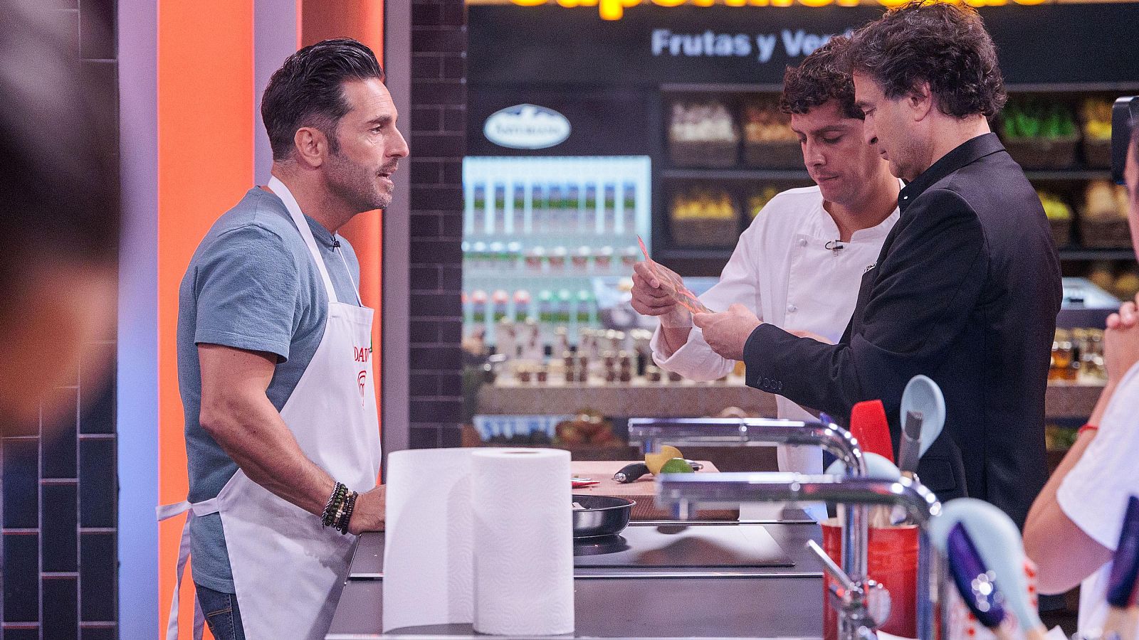 David Bustamante con delantal blanco y el chef Pepe Rodríguez observan una lámina transparente en una cocina de MasterChef.