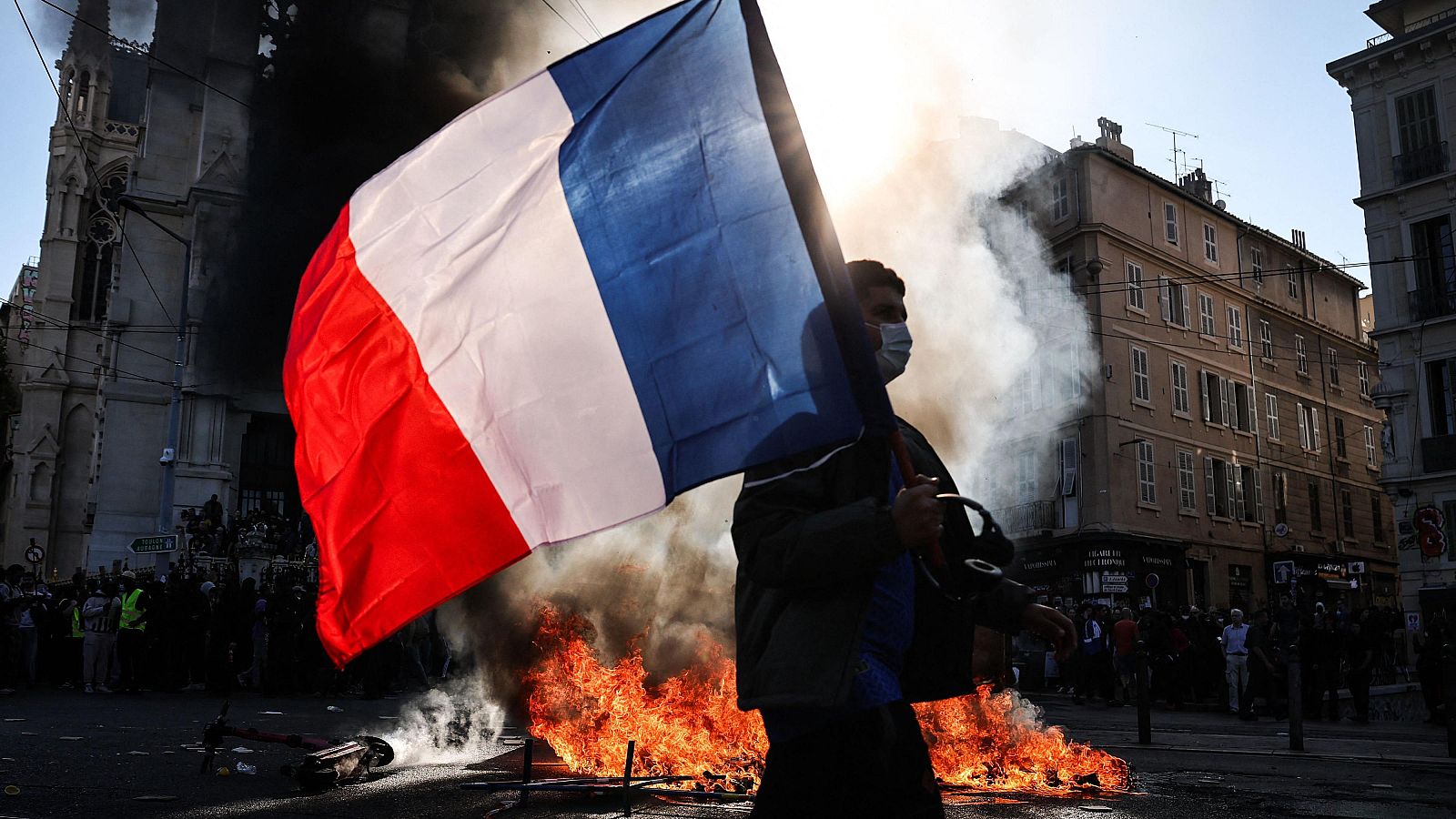 Manifestante con la bandera francesa en Marsella pasa junto a una barricada en llamas durante unos disturbios urbanos.