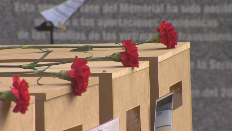 Primer plano de urnas de madera clara con claveles rojos y fotograf�as de v�ctimas en un acto de memoria hist�rica.