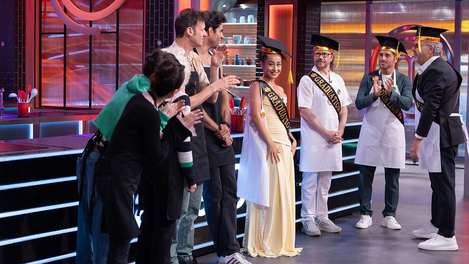 Marina Rivers con vestido amarillo y birrete de graduación es ovacionada por compañeros y veteranos en el plató de MasterChef Celebrity.