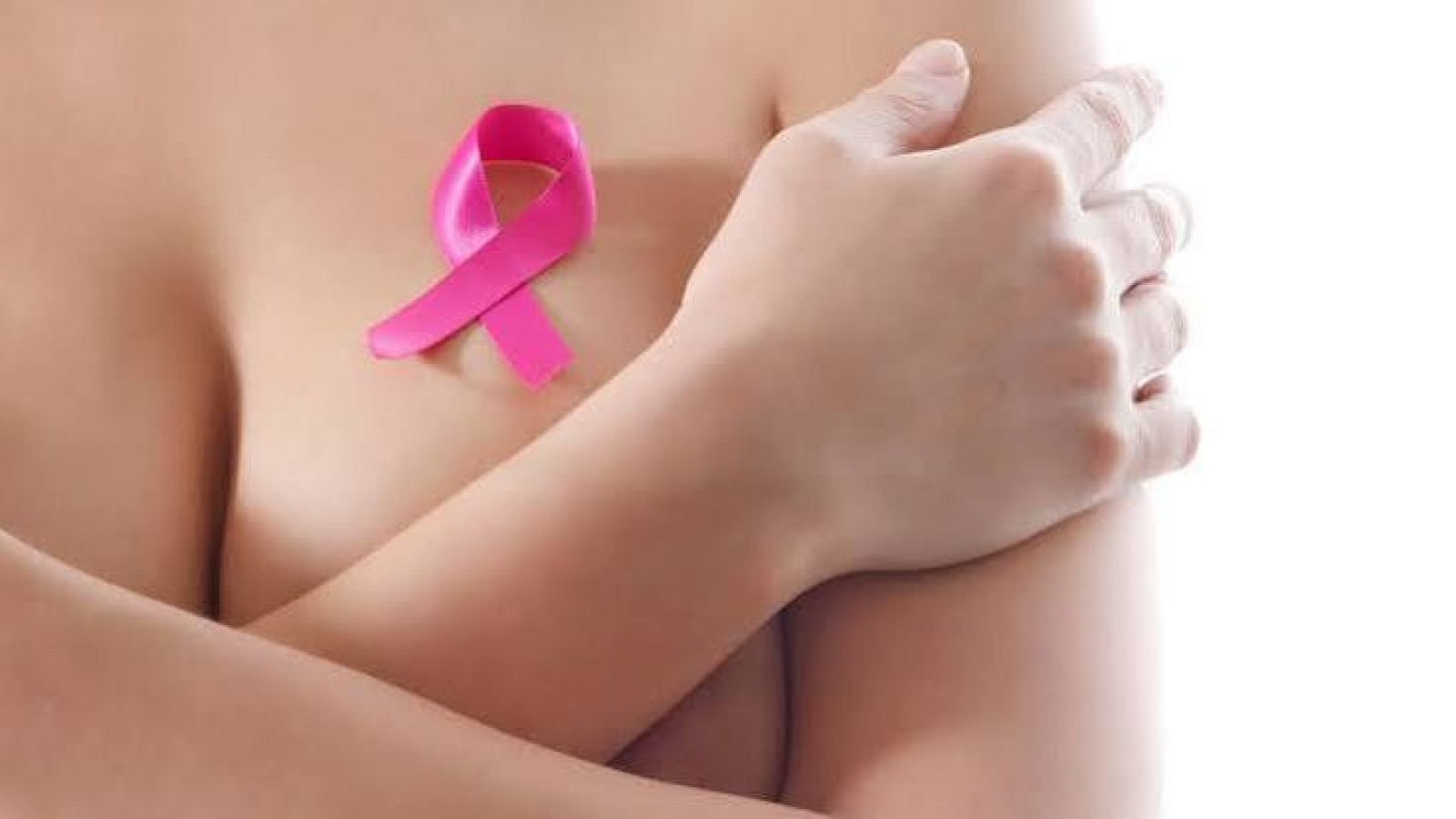 Primer plano de una mujer con los brazos cruzados sobre el pecho y un lazo rosa de concienciación contra el cáncer de mama sobre su piel.