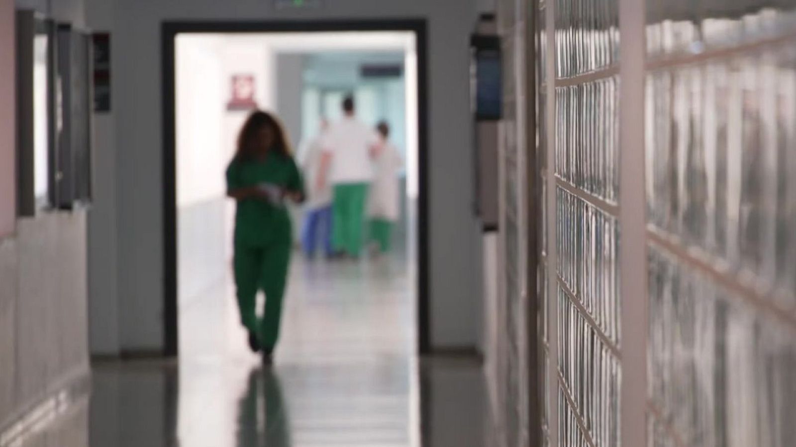 Pasillo de hospital con suelo brillante y figuras de personal sanitario desenfocadas al fondo.