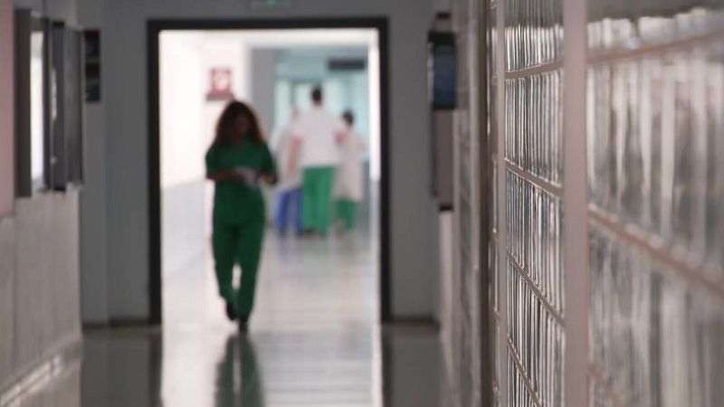 Pasillo de hospital con suelo brillante y figuras de personal sanitario desenfocadas al fondo.