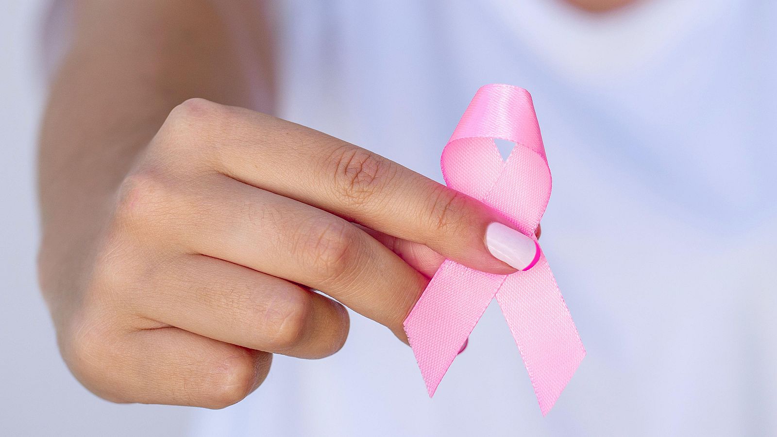 Primer plano de una mano sosteniendo un lazo rosa brillante, símbolo de la concienciación sobre el cáncer de mama, con fondo difuminado.