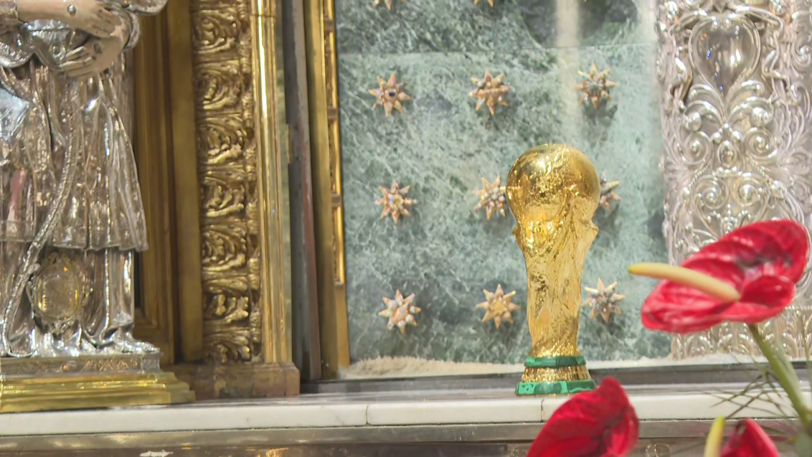El trofeo de la Copa del Mundo de la FIFA se muestra sobre una repisa junto a detalles barrocos, orfebrería de plata y decoración floral en un interior religioso.