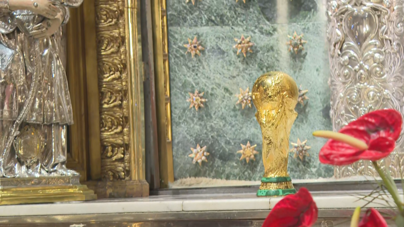 El trofeo de la Copa del Mundo de la FIFA se muestra sobre una repisa junto a detalles barrocos, orfebrería de plata y decoración floral en un interior religioso.