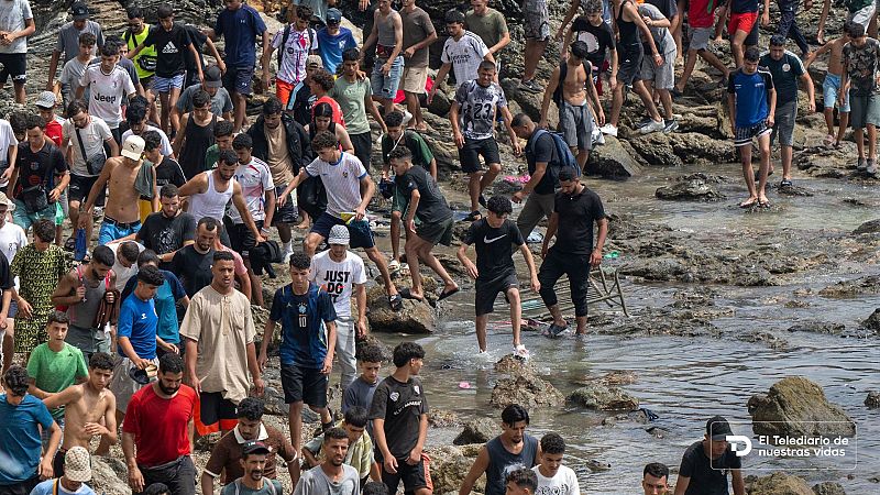 Multitud de jóvenes avanzan a pie por una costa rocosa y resbaladiza junto al mar en una crisis migratoria
