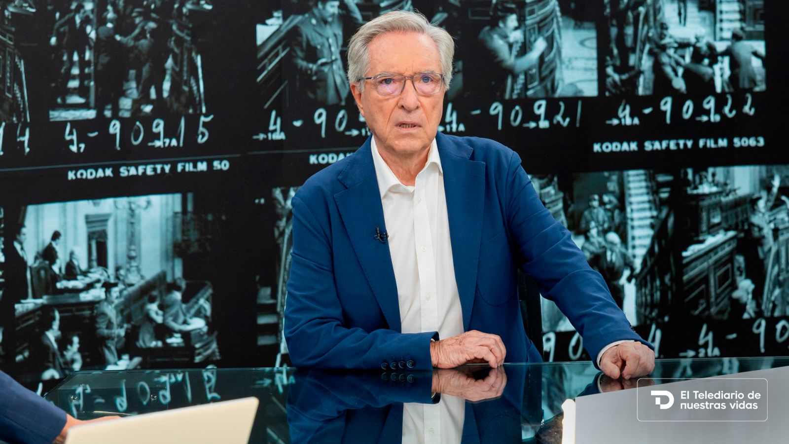 El periodista Iñaki Gabilondo en un plató televisivo con una mesa de cristal y fondo de imágenes históricas del 23-F.