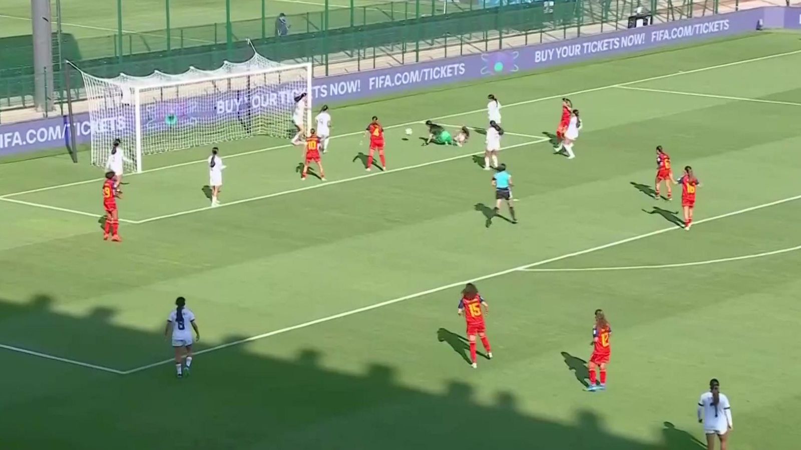 Jugada de peligro en el área de penalti durante un partido de fútbol con jugadoras rojas y blancas, y la portera en el suelo.