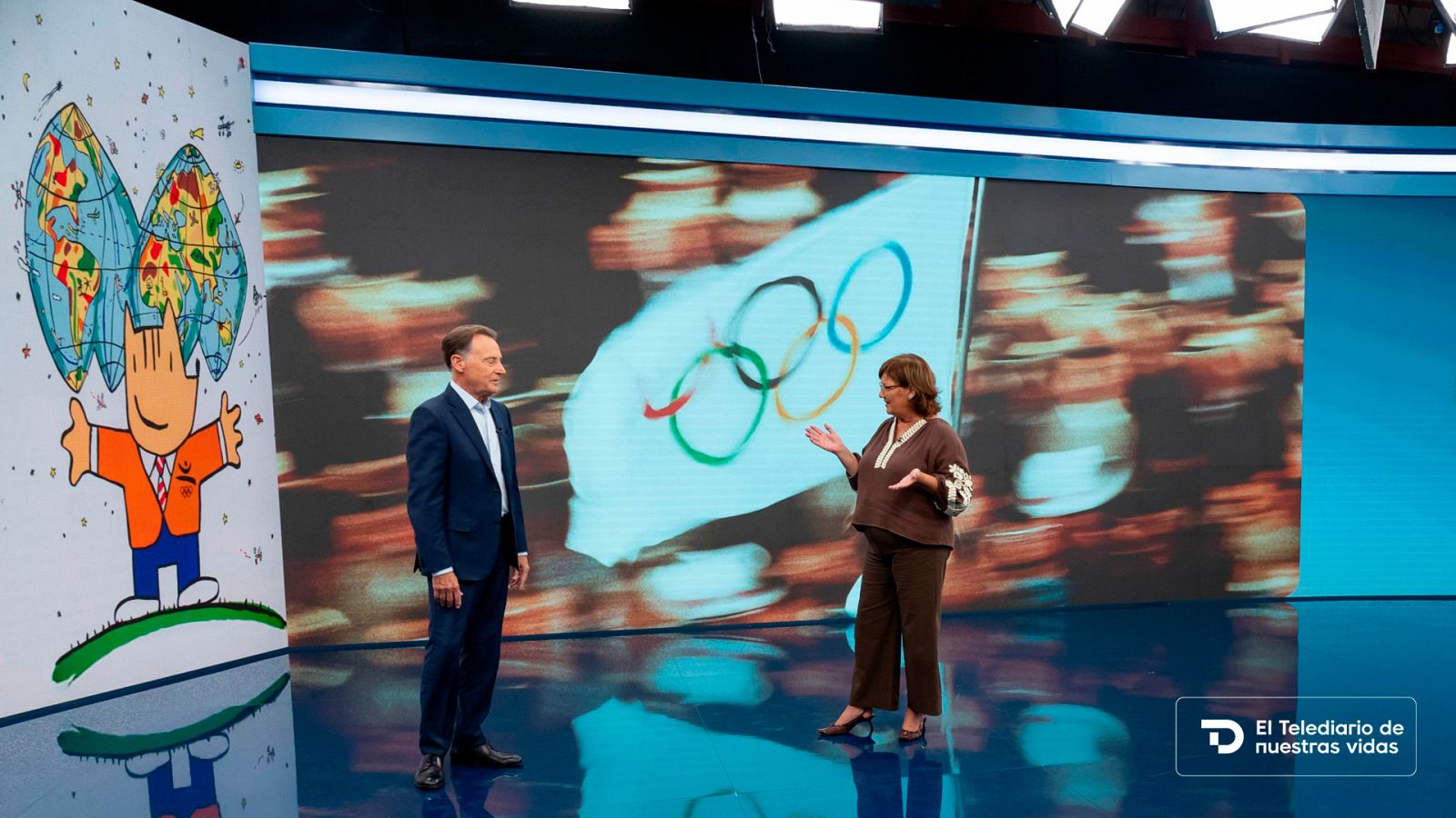 Los periodistas Jesús Álvarez y Ana Blanco en el plató de informativos con la bandera olímpica de fondo y un gráfico del programa en pantalla.