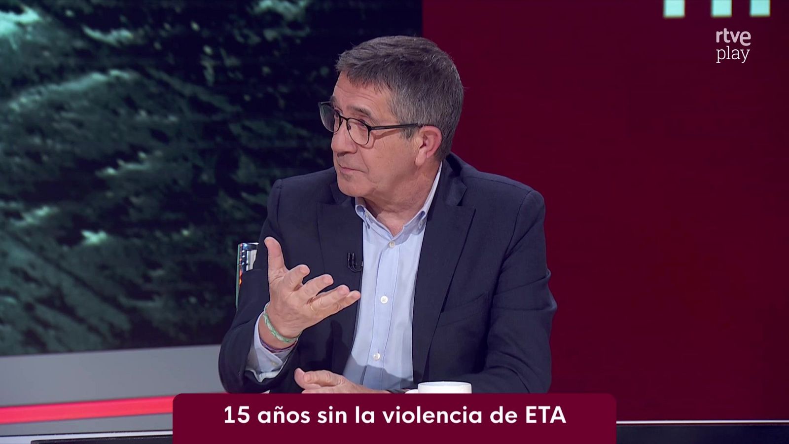 Un hombre con chaqueta azul y gafas gesticula en un plató de televisión con un rótulo sobre la violencia de ETA.