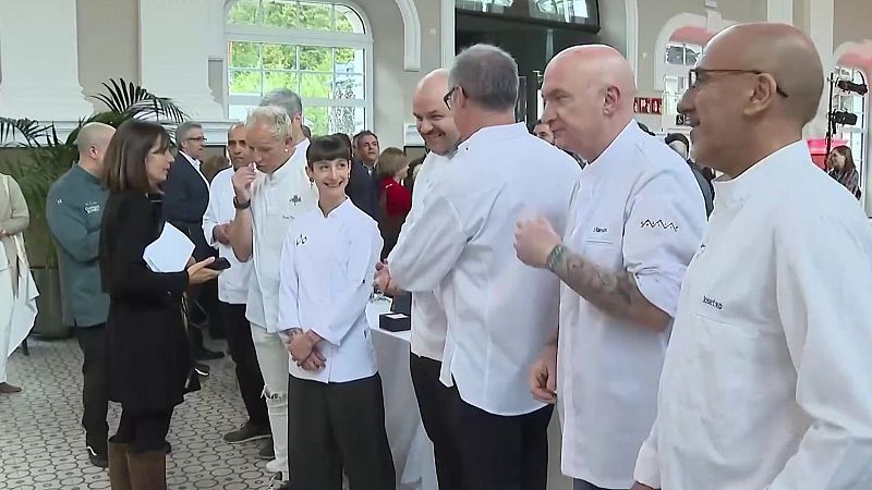 Varios chefs galardonados de Aragón con chaquetilla blanca conversan en el vestíbulo histórico de la Estación de Canfranc durante un encuentro gastronómico cubierto por la prensa.