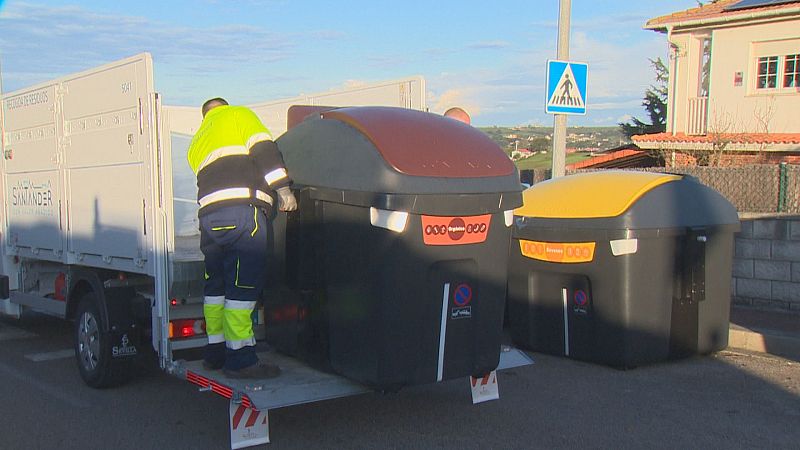 Operarios municipales instalan contenedores de reciclaje desde un camión blanco en una calle residencial.