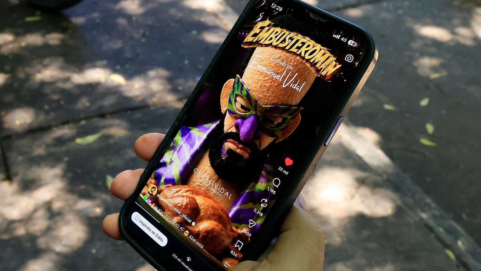 Primer plano de una mano joven sujetando un smartphone al aire libre, mostrando una red social de vídeos con una marioneta.