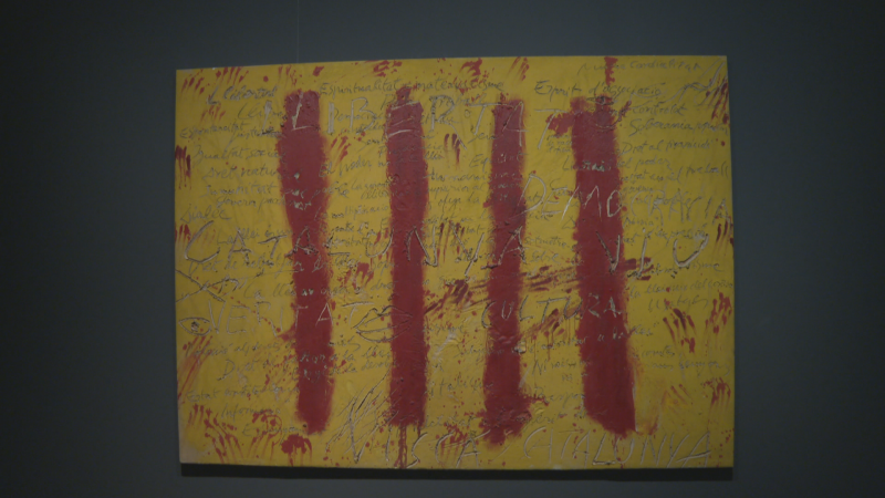 Pintura matérica con fondo ocre y bandas rojas verticales que recuerdan a la senyera, con inscripciones como 'LLIBERTAT' y 'CATALUNYA' sobre superficie texturizada.