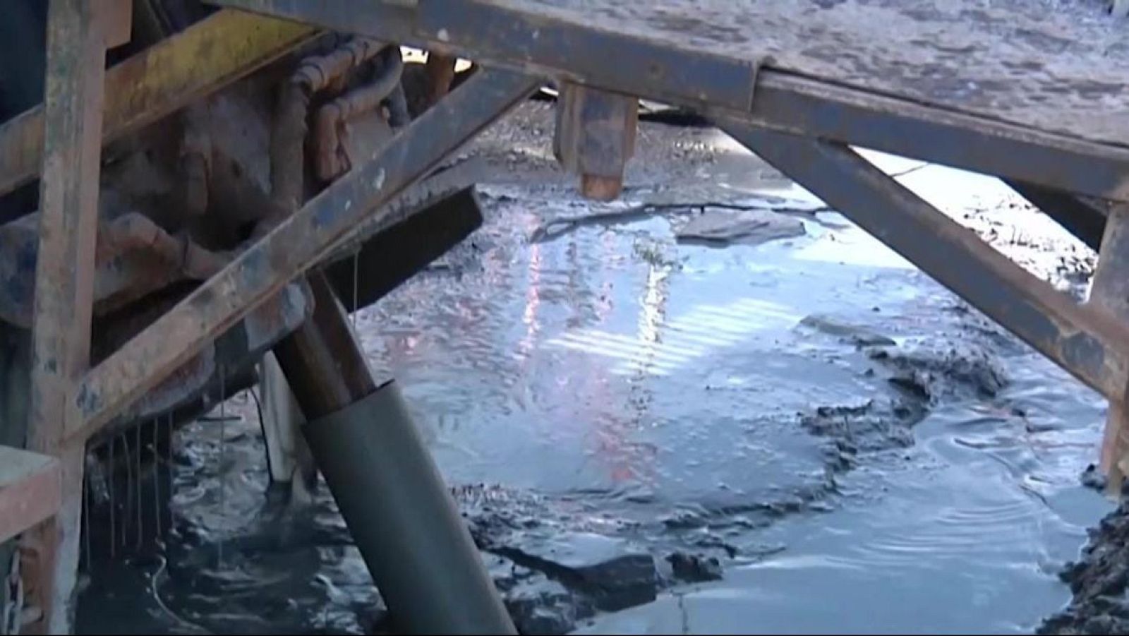 Maquinaria de perforación industrial operando sobre un terreno enfangado con montículos de tierra.