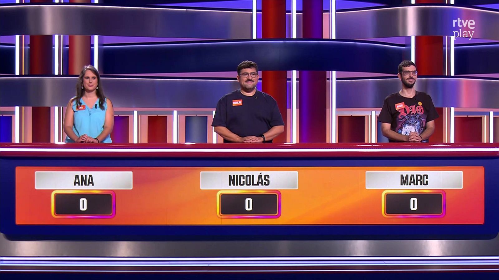 Tres concursantes de pie tras un mostrador iluminado en un plató de televisión, con marcadores a cero y el logotipo de rtve play visible.
