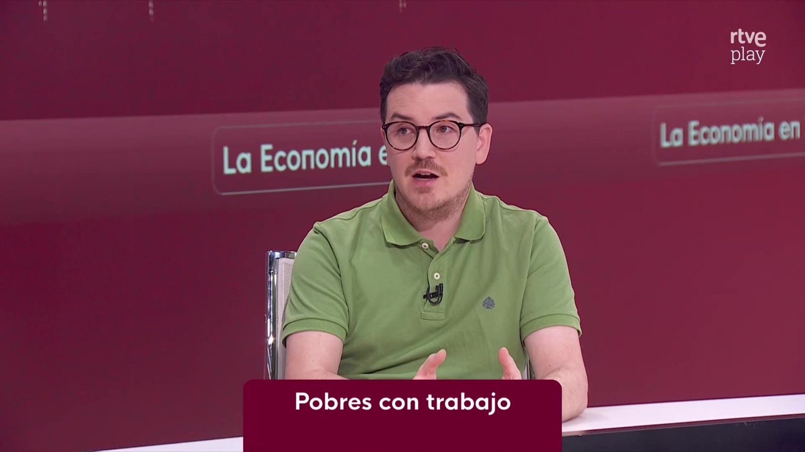 Hombre con gafas y polo verde gesticula en un plató de RTVE durante un programa de debate con el rótulo «Pobres con trabajo».