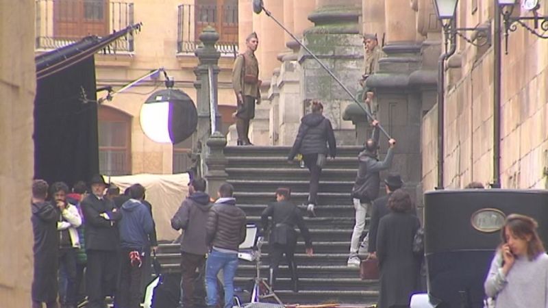 Plano general de un rodaje de época con actores en uniformes militares y trajes de los años 30 junto al equipo técnico frente a una escalinata monumental.