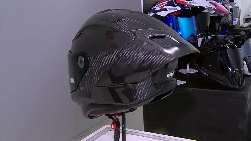 Casco integral de motocicleta de fibra de carbono brillante expuesto junto a otros cascos en una tienda.