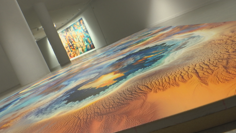 Sala de arte moderno con una obra escultórica de relieve topográfico en el suelo y una pintura abstracta al fondo.