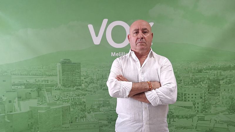 Plano medio de un hombre de mediana edad con camisa blanca y brazos cruzados frente a un panel corporativo verde con el logotipo de VOX.